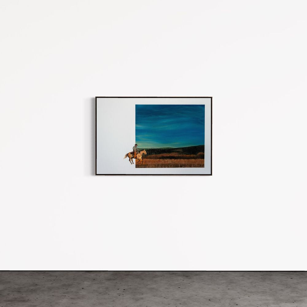 Framed artwork of a person on horseback against a blue sky, hanging on a white wall.