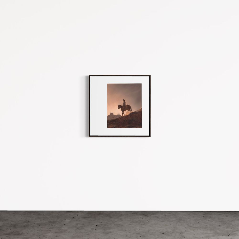 Framed artwork of a silhouette of a person on horseback against a sunset sky, hanging on a white wall.