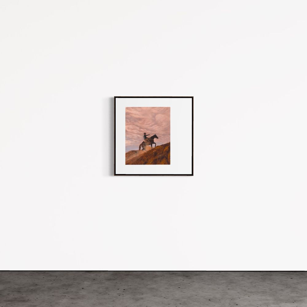 Framed artwork of a horse on a hillside against a pink sky, hanging on a white wall.