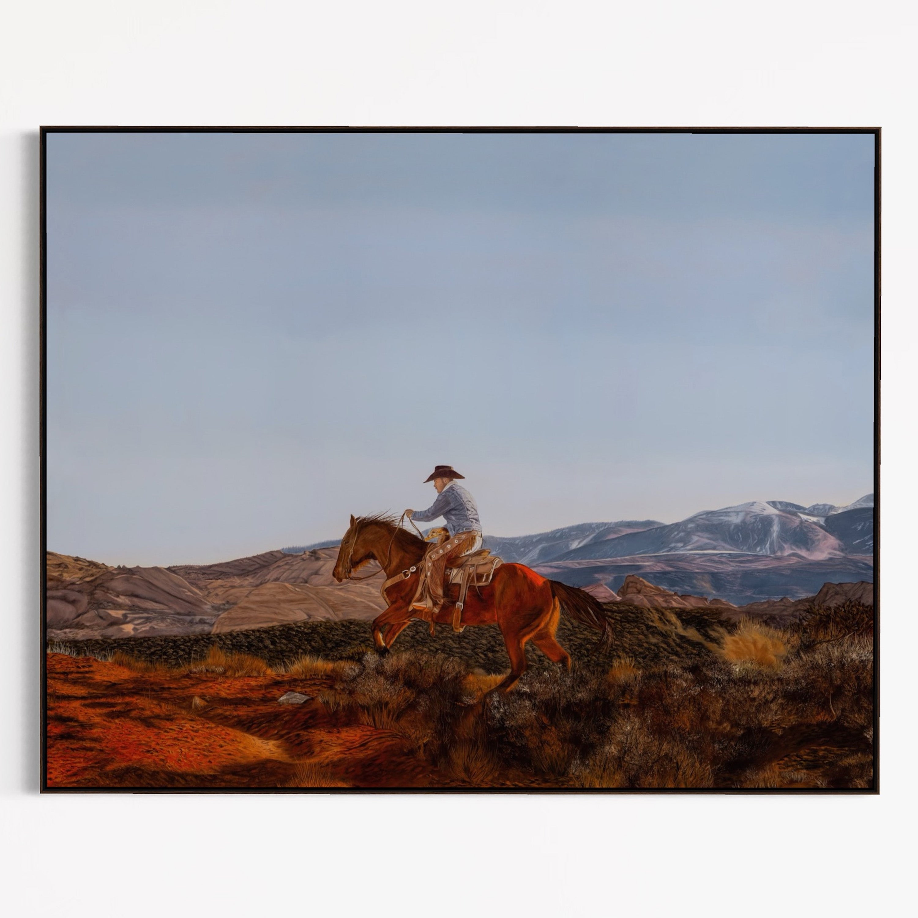 Framed artwork of a cowboy riding a horse with mountains in the background