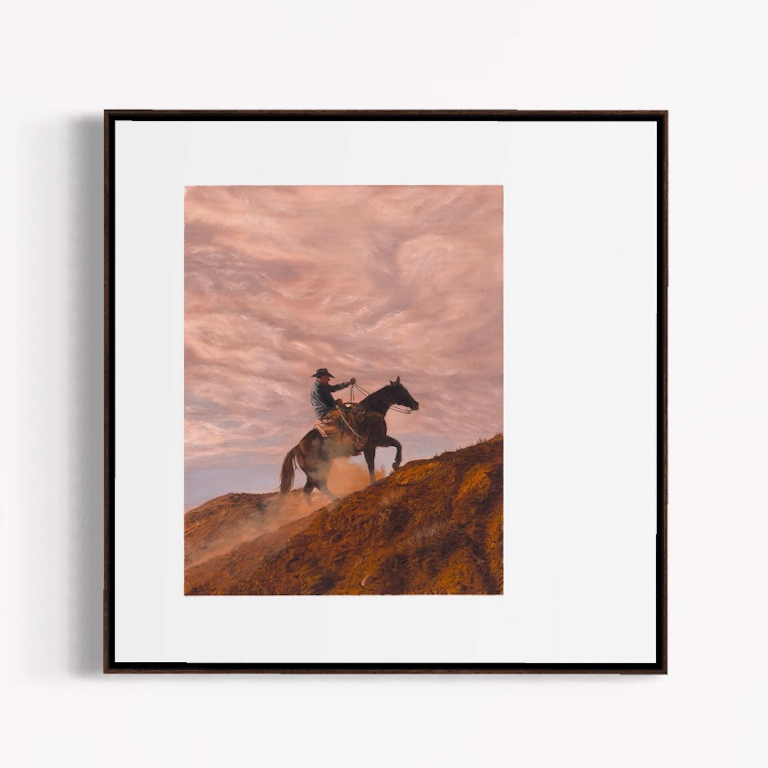 Framed artwork of a person riding a horse on a hill with a pink sky.
