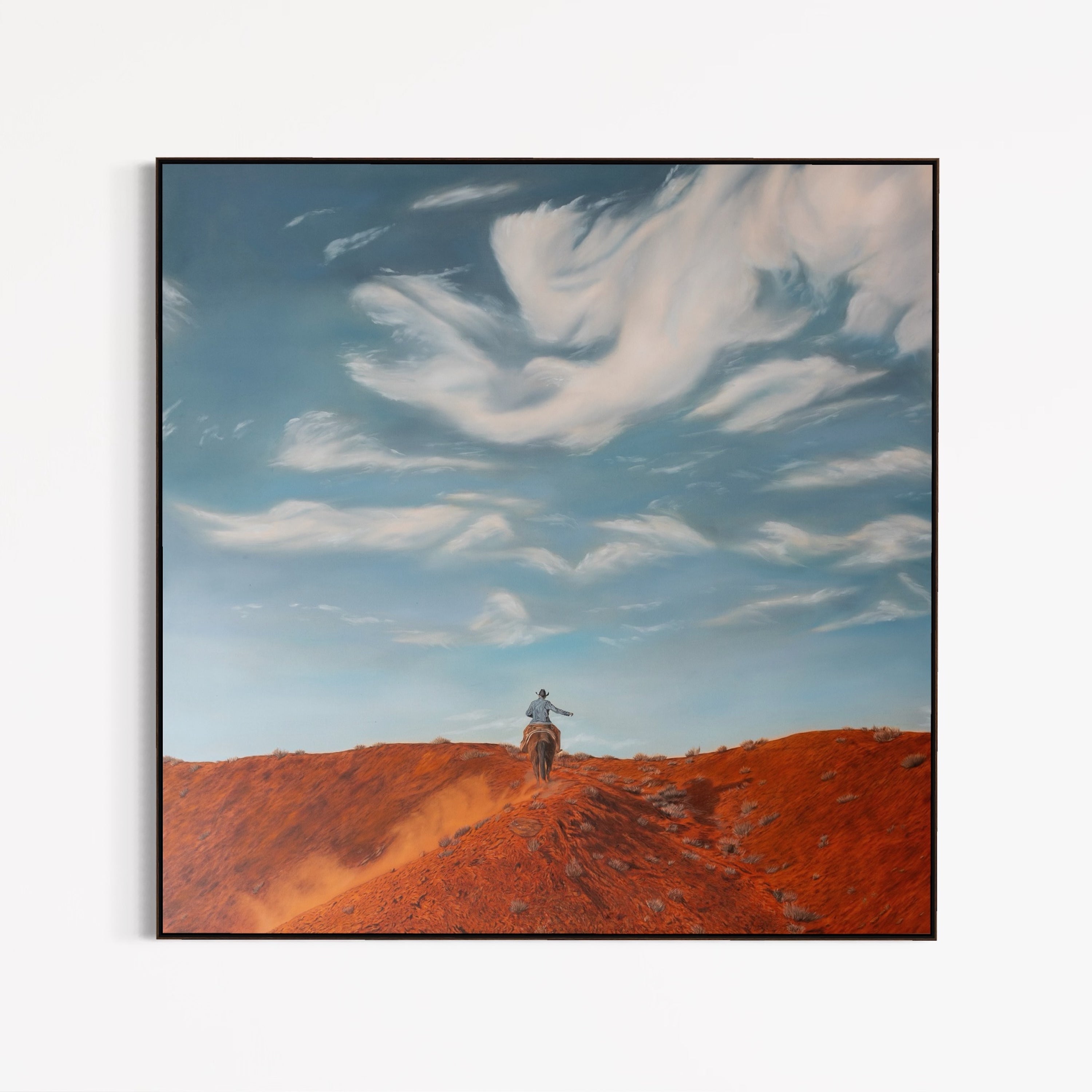 Framed artwork of a person on horseback in a desert landscape with a blue sky.