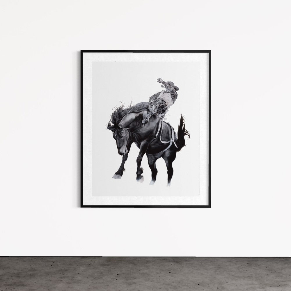 Framed black and white artwork of a horse and rider on a white wall.