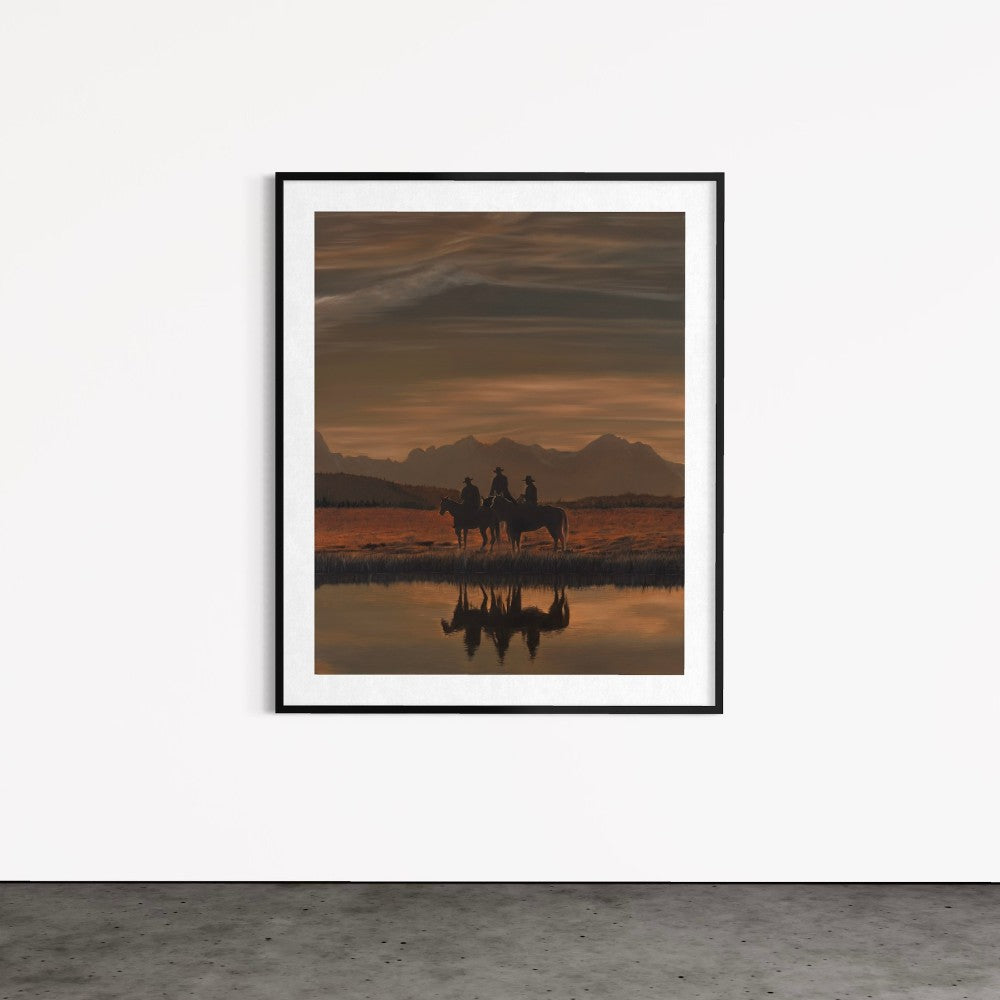 Framed artwork of two people on horseback at sunset reflected in water, on a white wall.