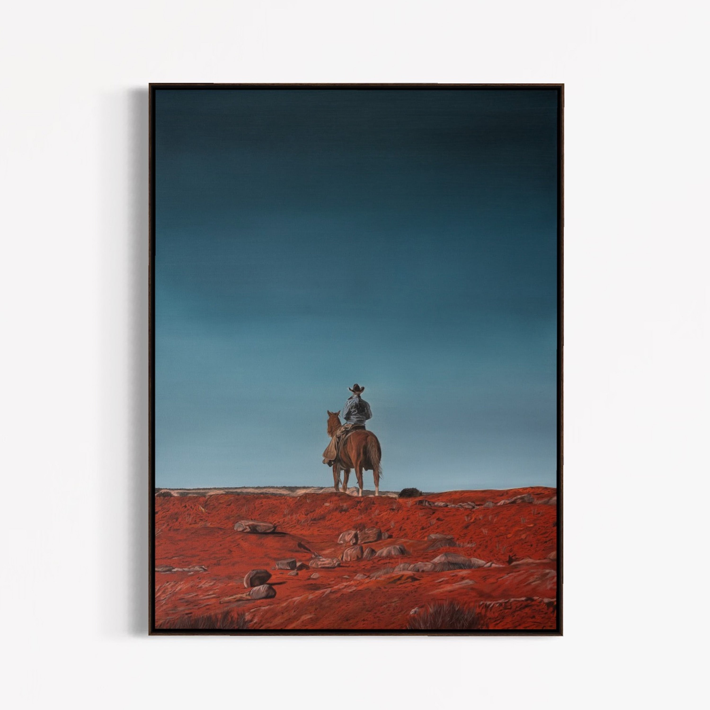 Framed artwork of a cowboy on horseback in a desert landscape with a blue sky.