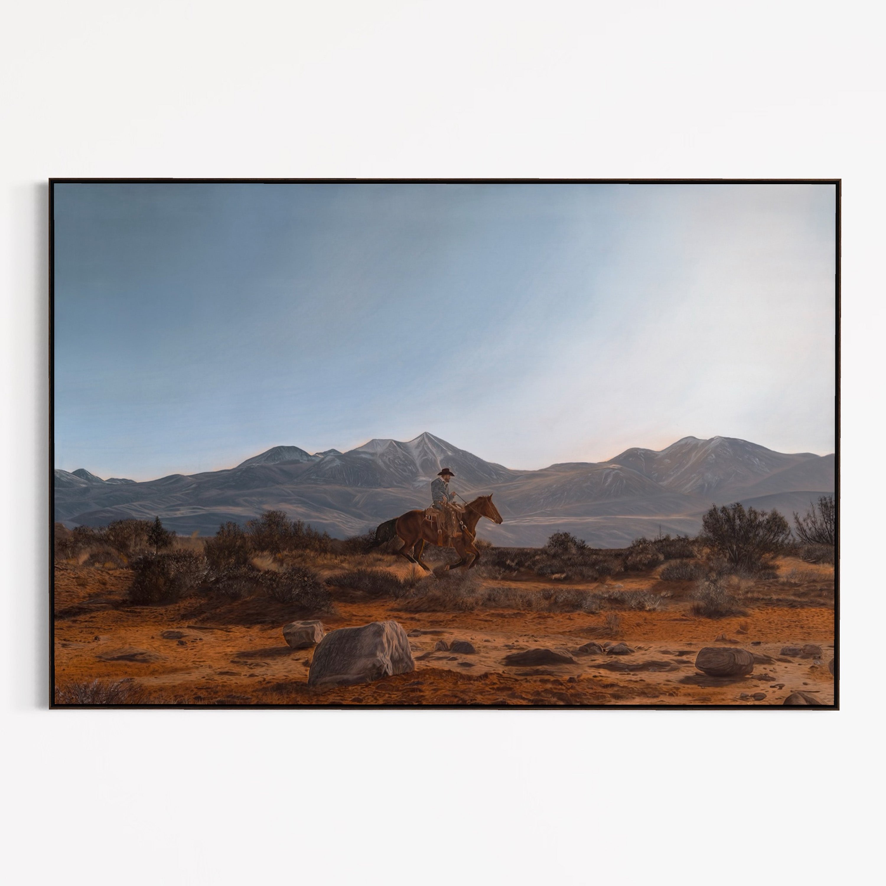 Person riding a horse in a desert landscape with mountains in the background