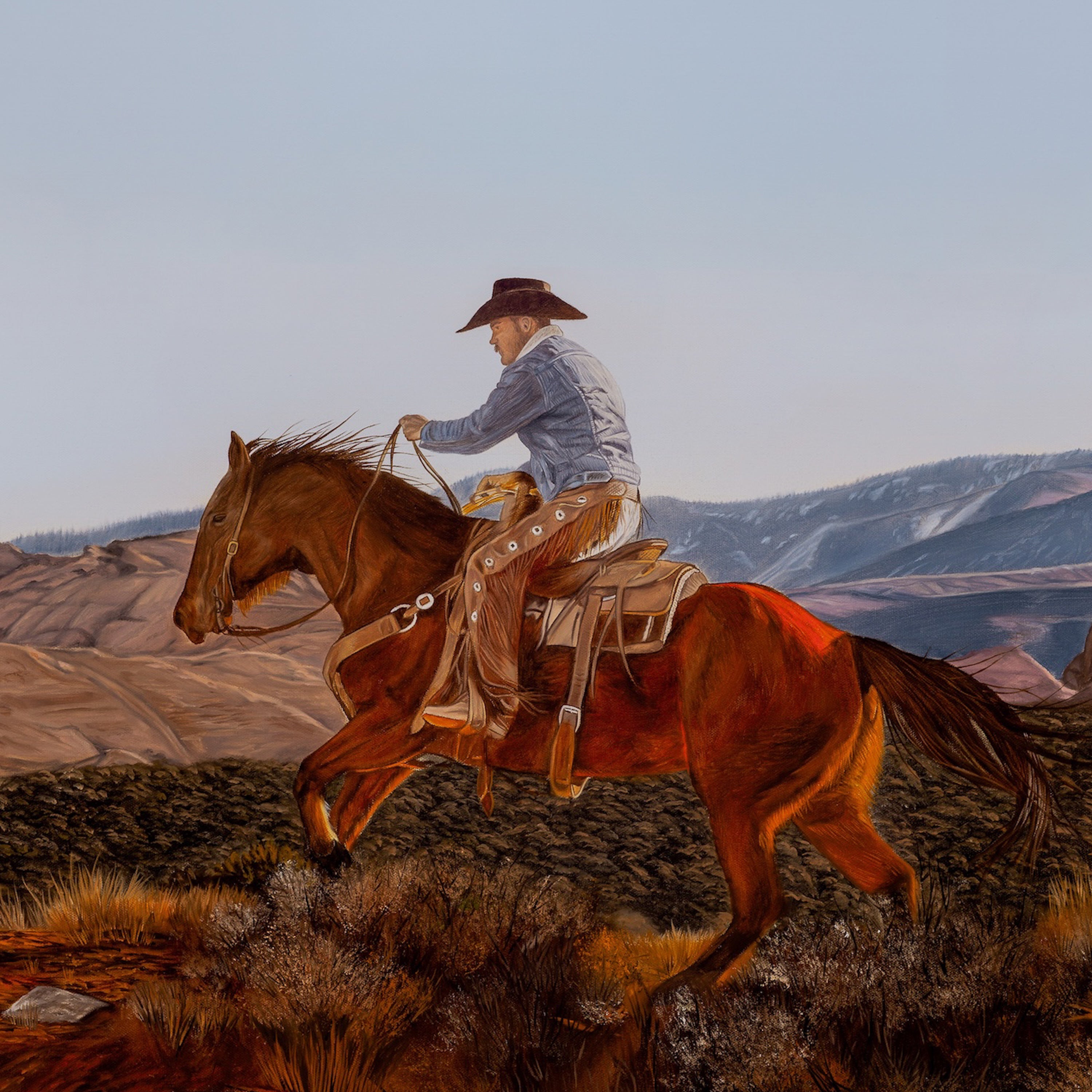 Man riding a horse in a desert landscape with mountains in the background