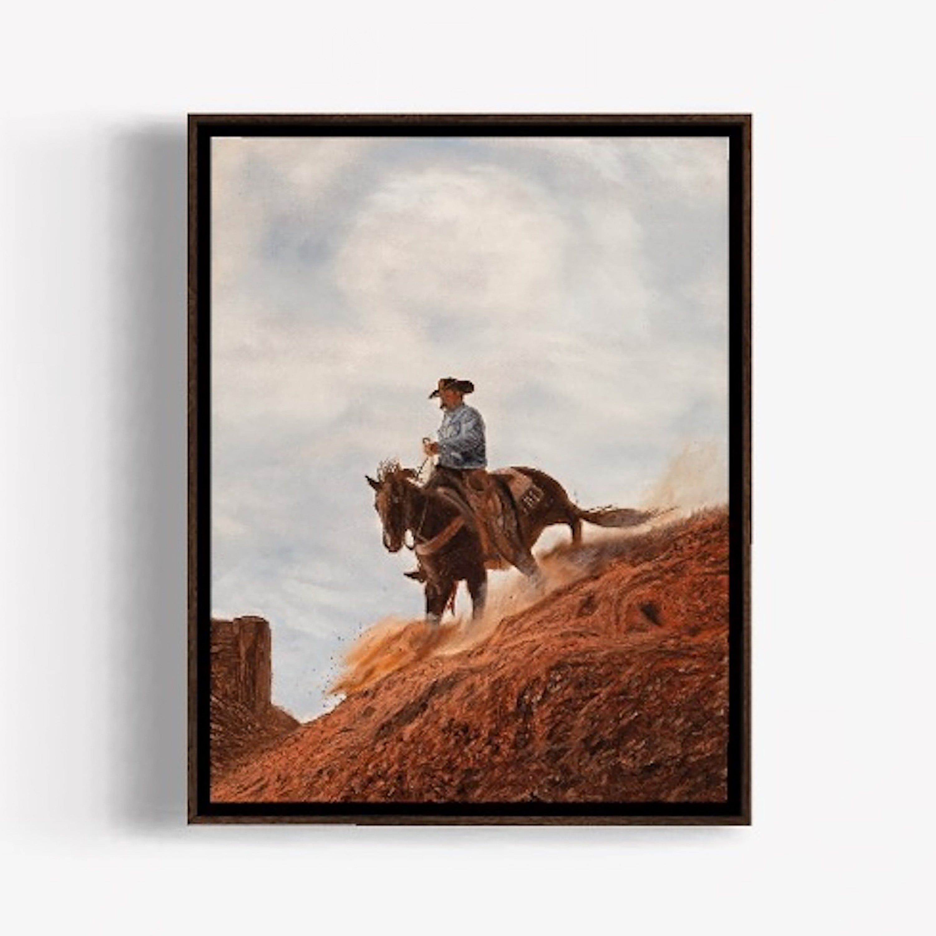 Framed artwork of a cowboy riding a horse on a dirt path with a cloudy sky.