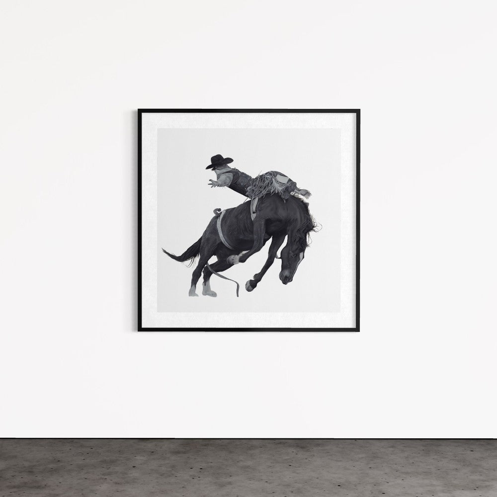 Framed black and white artwork of a person riding a horse on a white wall.