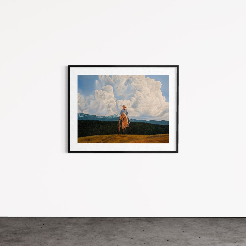 Framed artwork of a horse in a field with clouds and mountains on a white wall.