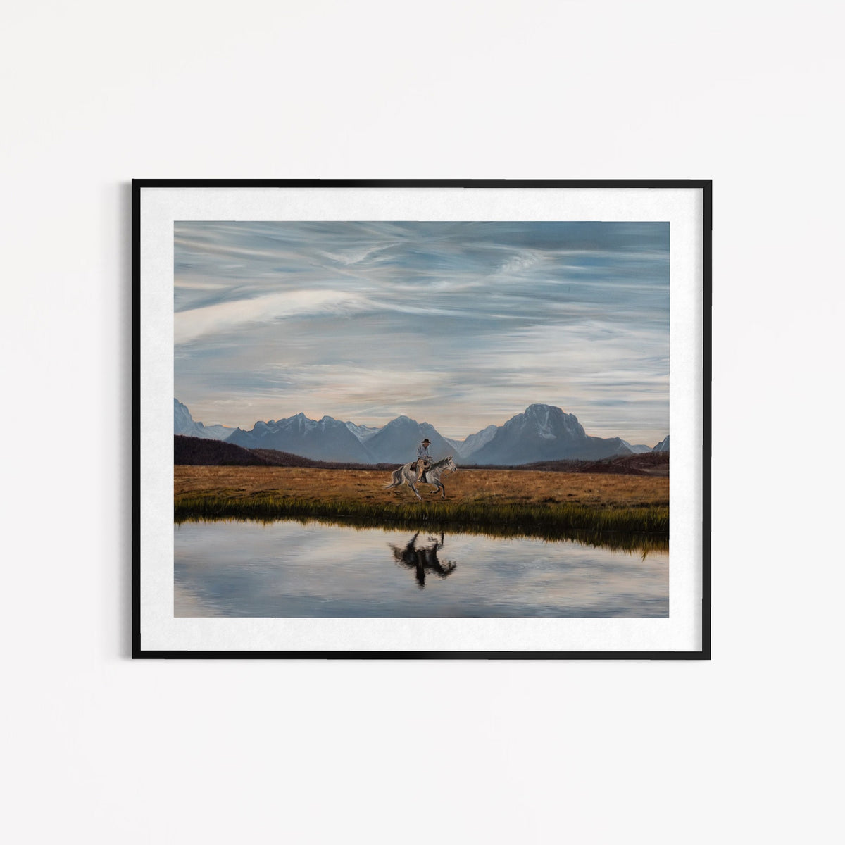 Framed artwork of a person riding a horse near a reflective lake with mountains in the background.